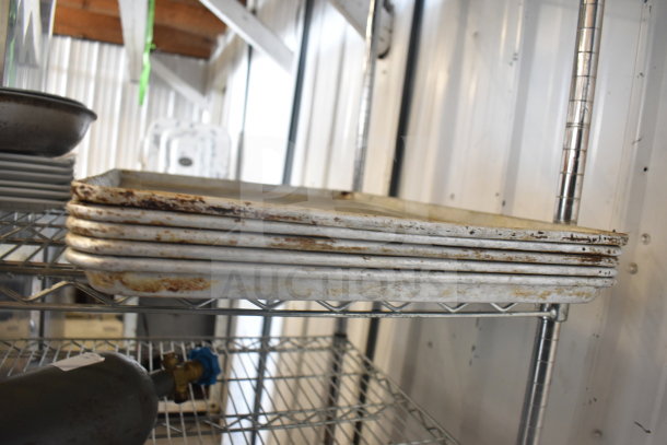 Stacked baking pans with visible rust on metal shelves in industrial setting. Part of assorted kitchenware lot.