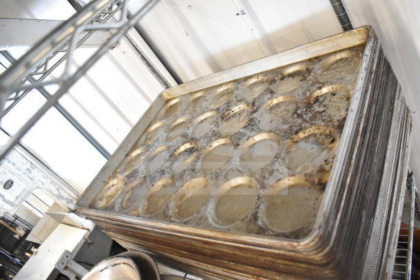 Stack of used baking pans with round indentations, showing signs of wear, part of mixed lot with colander and plates.