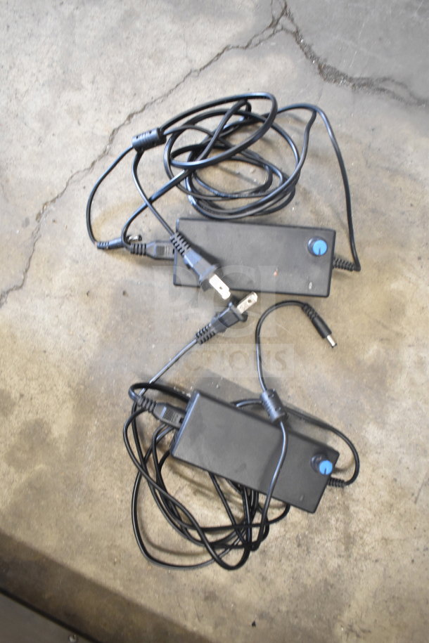 Two power adapters with attached cables on a concrete surface, featuring standard plugs and connectors.