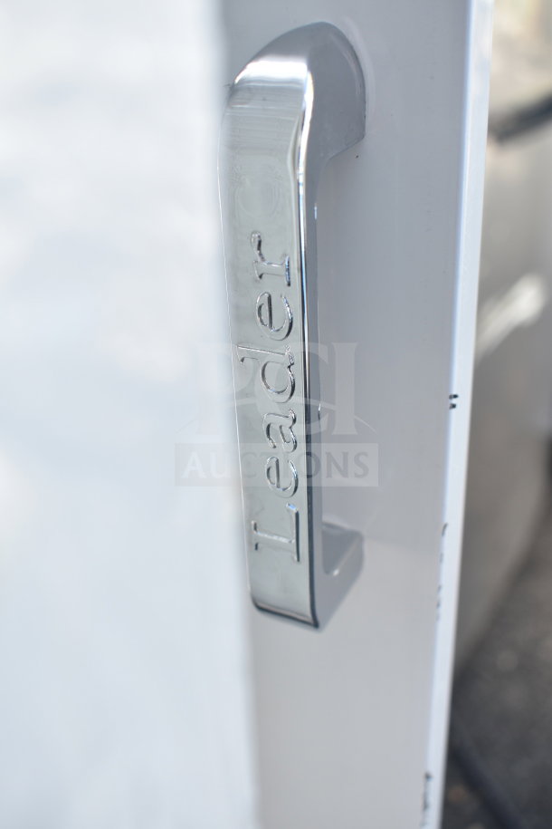 Close-up of a "Leader" branded silver handle on a white surface, possibly indicating a refrigeration unit or similar appliance.