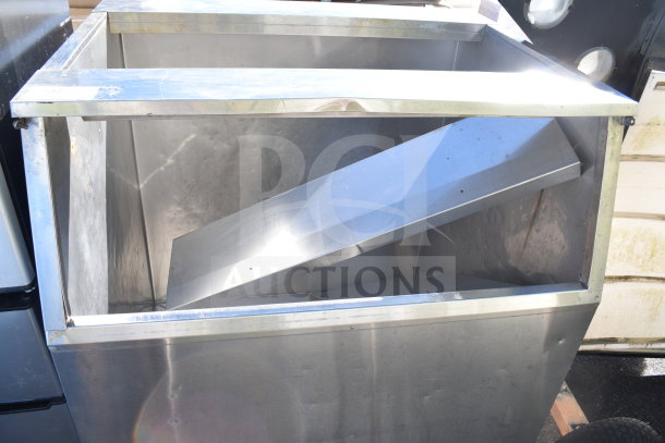 Commercial ice machine bin with metallic finish, open top, slight wear, and sturdy construction. Ideal for high-volume use.