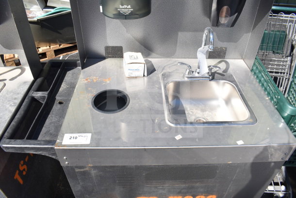 Commercial portable sink on casters, stainless steel basin, faucet, soap dispenser, and waste compartment. Shows some rust and wear.