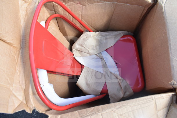 Red chair in a box, partially wrapped, labeled as scratch and dent condition, appears new with protective packaging.