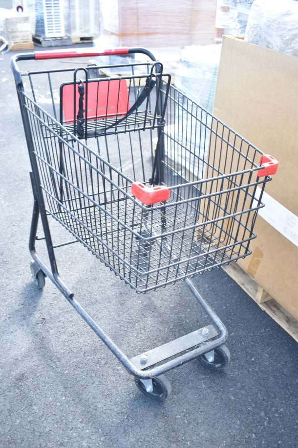 Metal shopping cart with a red handle and seat, in good condition, on a warehouse floor.