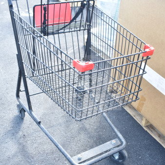Metal shopping cart with a red handle and seat, in good condition, on a warehouse floor.
