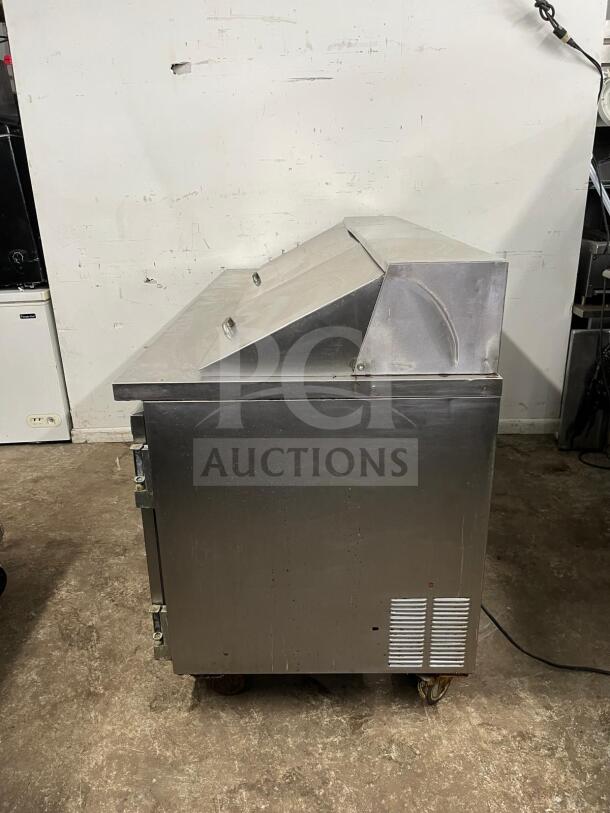 LEADER NSFM72 72" 3-door mega top refrigerated prep table, stainless steel, side view, some wear, on caster wheels.