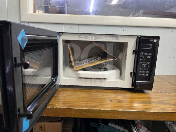 Insignia NS-MW07BKO 0.7 Cu. Ft. compact countertop microwave in black, open, showing control panel and interior packaging.