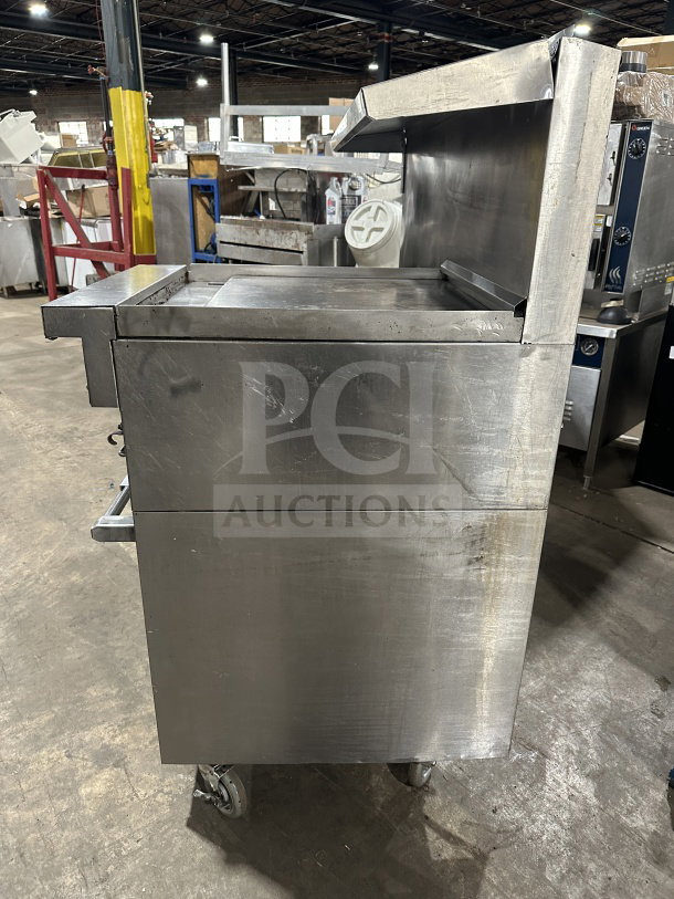 Commercial stainless steel 6-burner gas range with grille and two standard ovens on casters, industrial kitchen setting.