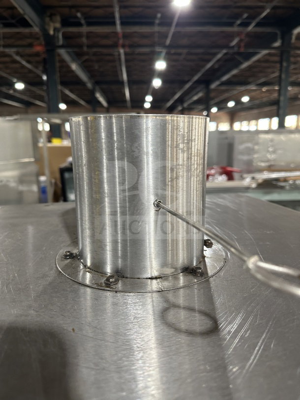Commercial stainless steel smoker oven with galvanized interior and legs. Close-up of chimney detail in warehouse setting.