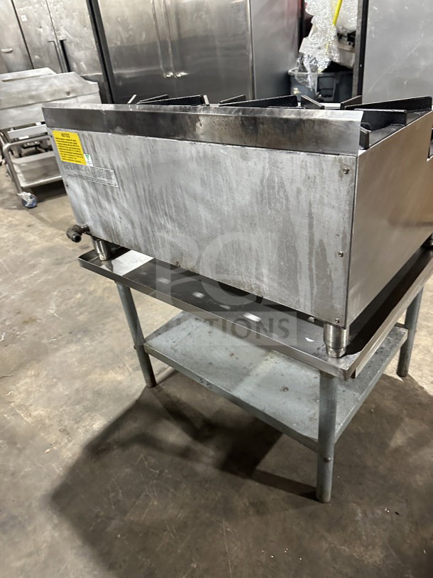 UltraMax stainless steel 6-burner gas hot plate on metal equipment stand. Industrial setting. Includes safety labels.