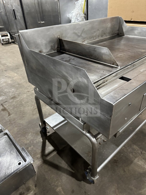 Commercial stainless steel gas-powered flat-top thermostatic griddle with integrated divider and stand on casters.