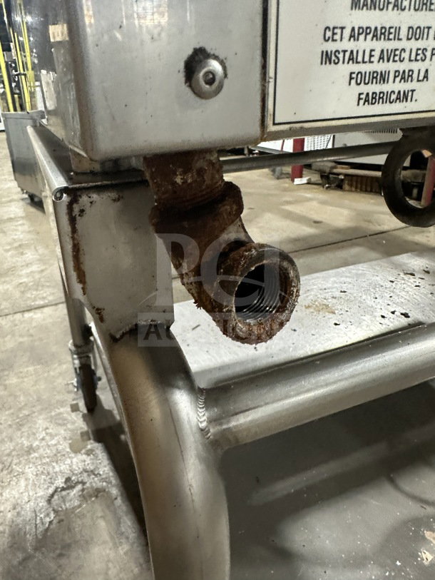 Commercial stainless steel flat-top griddle with integrated divider and stand. Visible rust on pipe. On casters for mobility.