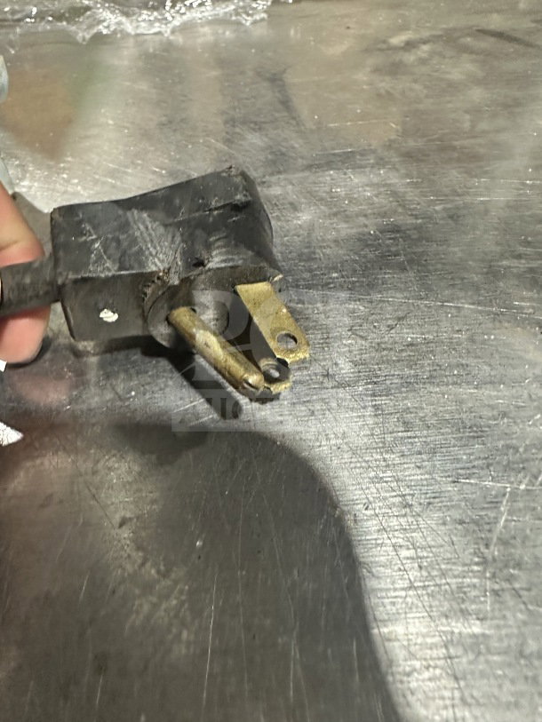 Close-up of a Beverage-Air refrigerator's power plug against a stainless steel surface, showing wear and scratches.