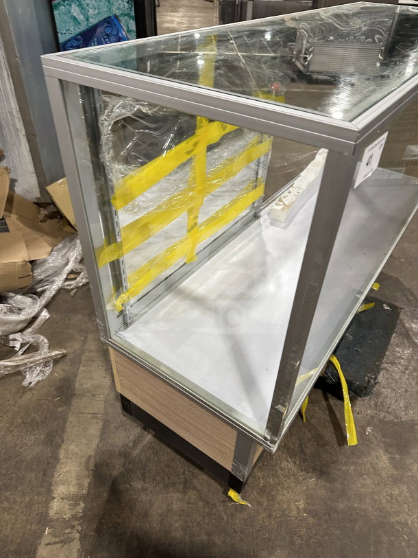 Commercial full glass dry bakery display case with wood grain trim, pristine condition, sturdy metallic frame, protective wrap present.