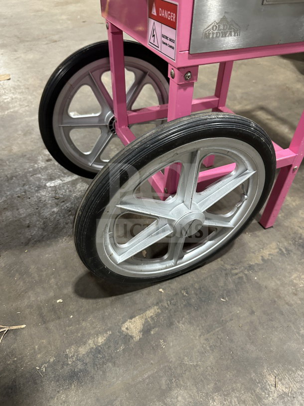 Olde Midway Spin-2000 cotton candy cart with pink frame, large wheels, stainless steel body, and safety markings.