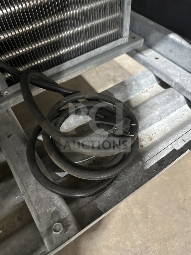 Coiled power cord near the base of a Leader stainless steel refrigerated salad bar, showing a metal cooling unit.