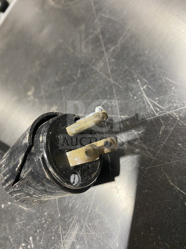 Close-up of a black electric plug on a metallic surface, showing wear and minor scratches.