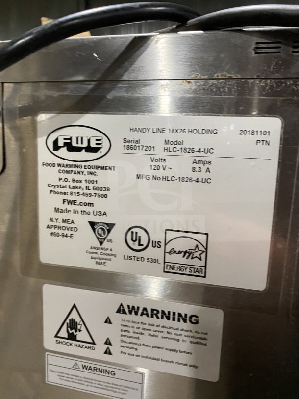 FWE Handy Line Series stainless steel 4-pan heated cabinet, model HLC-1826-4-UC, on casters, 120V, SN 186017201, shown with labels and warnings.