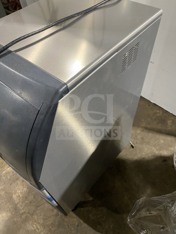 Scotsman commercial undercounter cube ice maker with built-in storage bin, on casters. Stainless steel exterior, power cord visible.