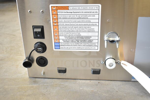 Back view of a brand new Fetco CBS-1252 Plus Series coffee brewer with warning and notice labels, switches, and power ports visible.