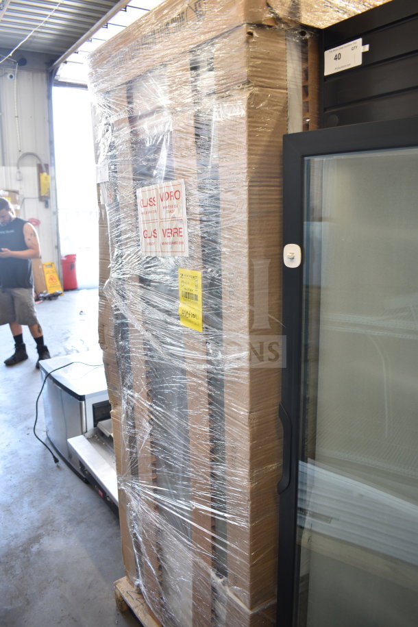 Pallet with shrink-wrapped large appliance labeled "GLASS VIDRO" and "HANDLE WITH CARE" in warehouse setting.