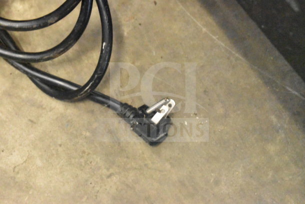 Black power cord for Avantco 178CFD1FF Commercial Freezer, 115 Volts, 1 Phase, showing three-prong plug on concrete floor.