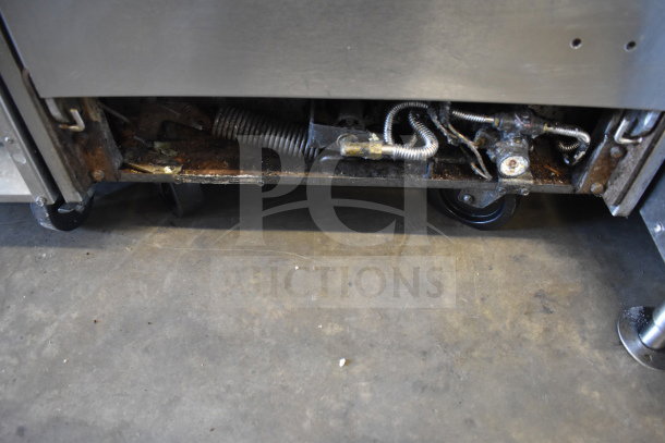 Commercial 4-burner gas range with oven, showing underside components and wheels, in used condition.