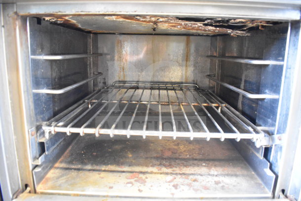 Inside view of a commercial gas-powered oven, showing metal racks and signs of use with rust and residue on surfaces.