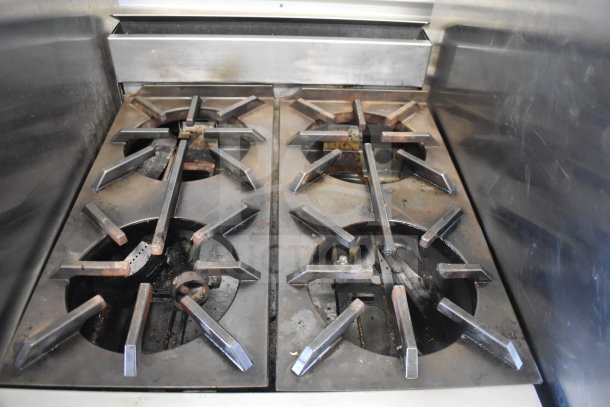 Commercial gas-powered range with 4 burners and oven, stainless steel, used condition, visible wear on burners.