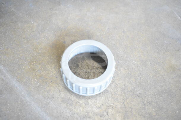 A close-up of a gray plastic threaded ring on a concrete floor, possibly part of a vacuum assembly.