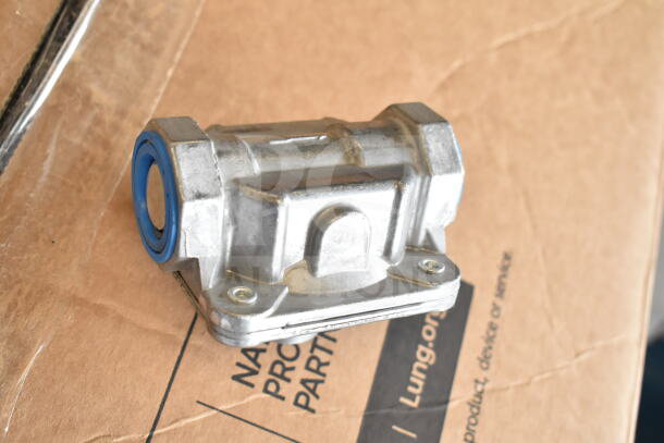 A small metal component with a blue seal, resting on cardboard packaging. No range is visible.