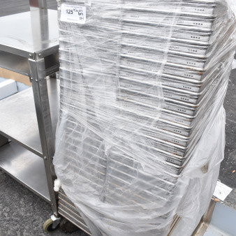 Stack of 64 metal baking pans wrapped in plastic, showing "Chicago Metallic" branding, indicating industrial quality.