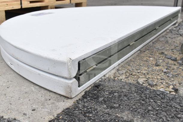 Brand new round bi-fold folding table with visible dents on edges, folded for storage, in scratch and dent condition.