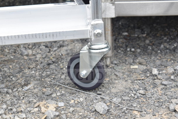 BRAND NEW Metal Pan Transport Rack with commercial casters on gravel. Slight scratches visible on metal frame.