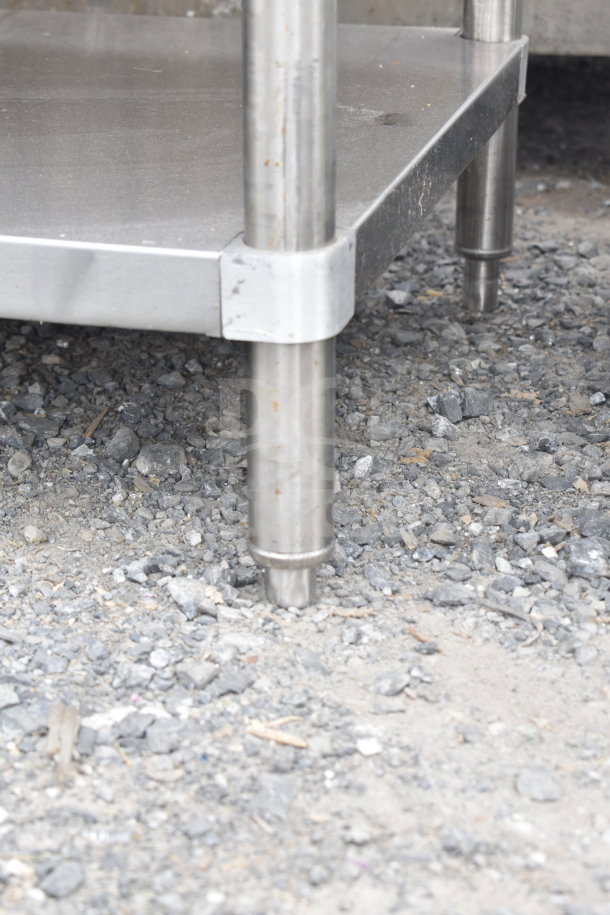 Stainless steel table with two under shelves, brand new with scratches and dents, sturdy metal legs, outdoor gravel base.
