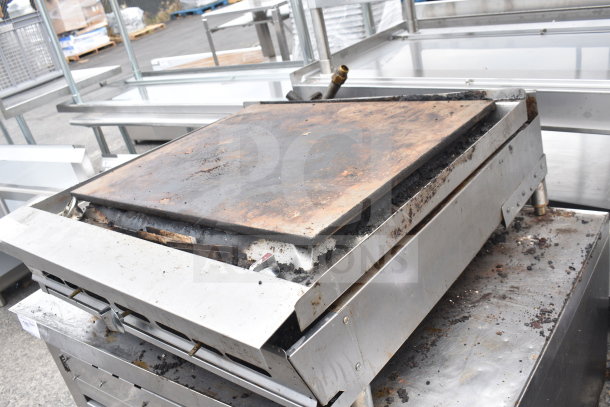 Commercial countertop gas-powered flat top griddle with visible wear, stainless steel frame, and adjustable knobs.