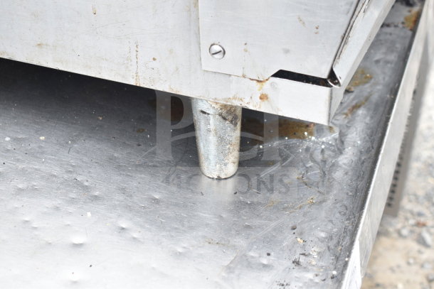 Commercial gas-powered flat top griddle, stainless steel, showing corner and supporting leg. Some signs of use visible.