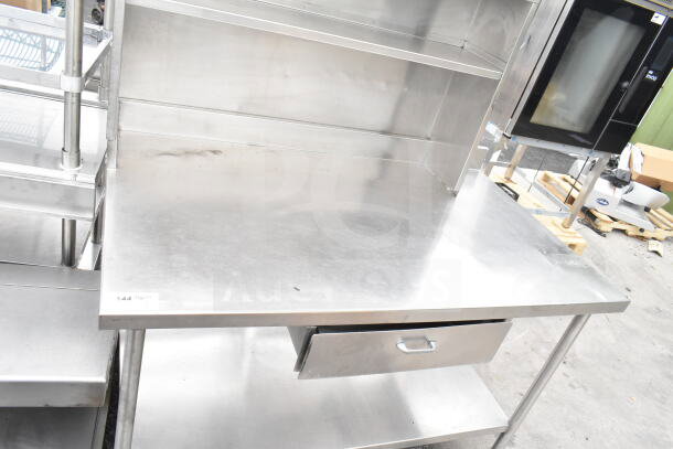 Stainless steel table with over shelf, drawer, and under shelf. Features durable design, numbered tag visible. Good condition.