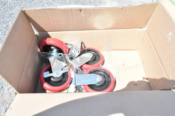Cardboard box containing several red and black caster wheels, part of a scratch and dent auction lot.