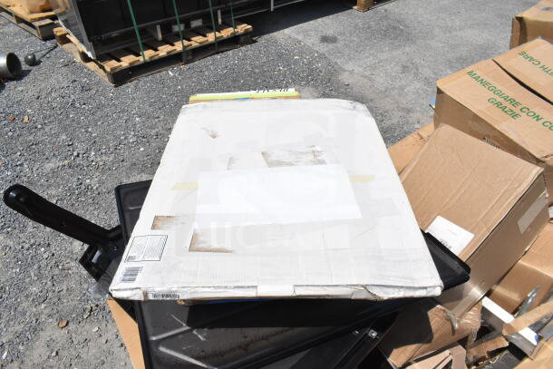 Boxes of new scratch and dent items, including speed rail, canopy tent, and serving trays, on a gravel surface.