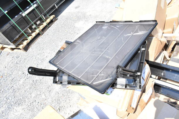 Image of a stack of black plastic serving trays, part of a scratch and dent auction lot. Trays show light wear and are placed on cardboard boxes.