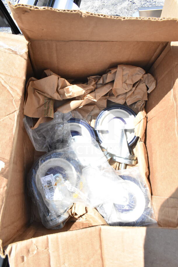 Box with new assorted casters, wrapped in plastic and brown paper. Part of 18-item scratch and dent auction lot.