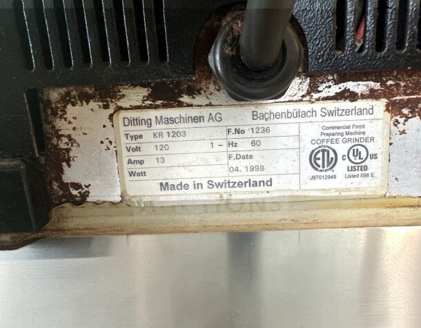 Tag on Ditting KR1203 coffee grinder showing model, voltage (120V), amp (13), Hertz (60), made in Switzerland, dated 04/1998.