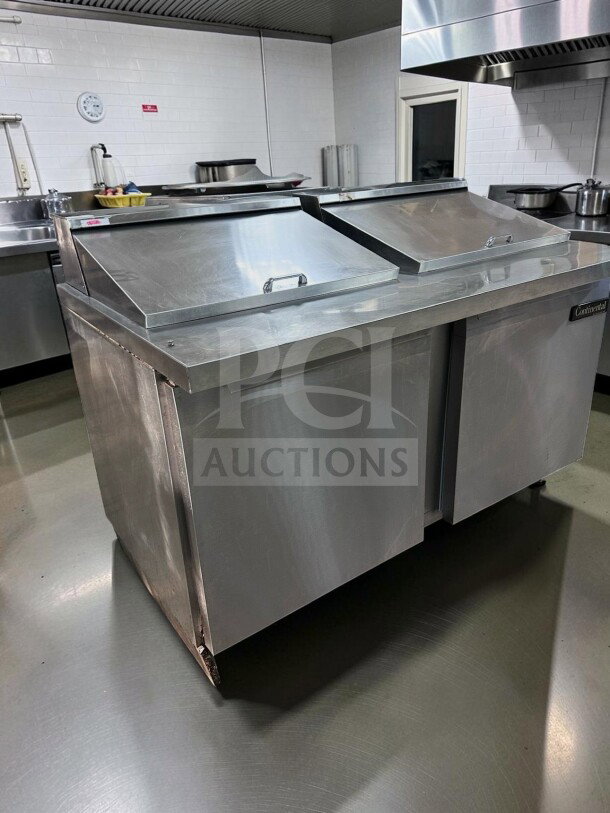 A stainless steel commercial refrigeration unit in a kitchen setting with two closed top lids and visible branding.