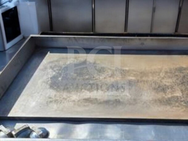 Commercial flat-top grill with worn surface, model Globe GG48G, showing signs of use. Made from stainless steel.