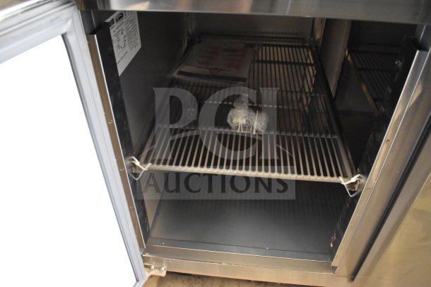 KoolMore KM-RPPS-2D59-GRT refrigerated pizza prep station interior, featuring stainless steel shelves and label, on commercial casters.