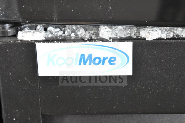 KoolMore logo on black surface with visible broken glass pieces, indicating damage to a commercial cooler.