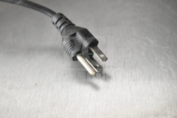 A black three-prong power plug on a commercial wrapping station with a metallic surface. Plug is part of a 115V setup.