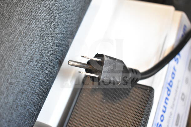 Store display showcasing sound bars and speakers with power plug detail, highlighting modern design and textured fabric.