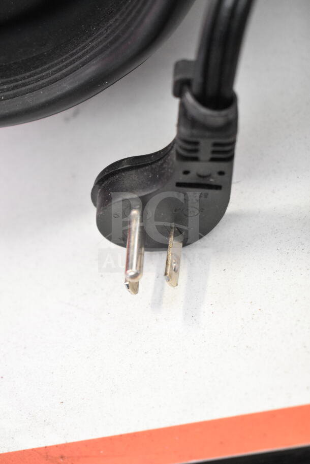 Close-up of a black electrical plug connected to a cable, resting on a white surface with red accents.